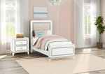 White bedroom set with bed, nightstand, and rug in a bright room. The Tiana Upholstered Twin Bedroom combines dazzling ambient LED lighting controlled by touch switches on all pieces. Choose from 7 colors to suit your mood. Dresser also features ball bearing drawer guides, felt lined top drawers with dovetail joinery and textured trim. 